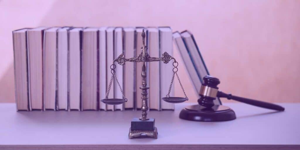 Vários livros de advocacia, uma balança da justiça e um martelo de juiz.